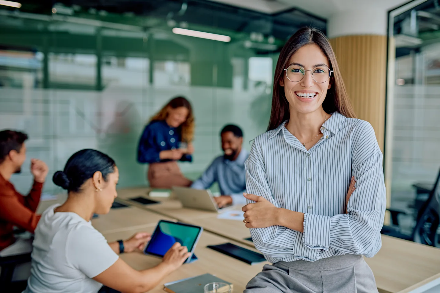 Lächelnde Frau mit Brille vor einem Team an einem Arbeitstisch im Büro